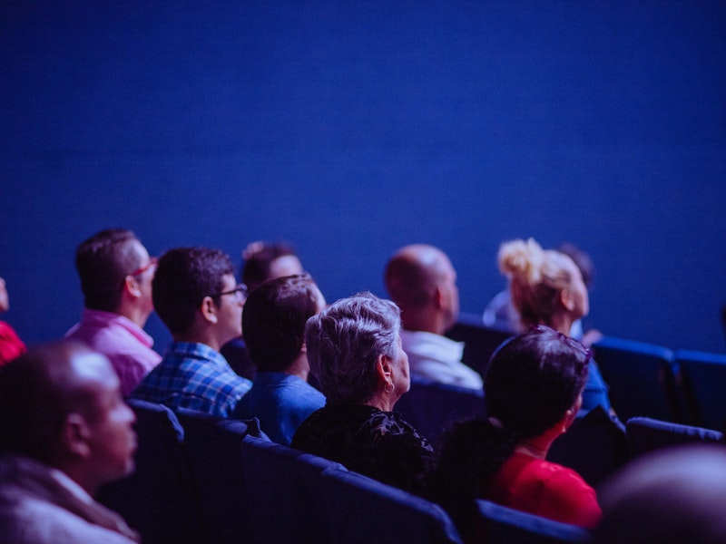 Imagen de varias personas que se encuentran de espaldas al objetivo, sentadas en un auditorio.